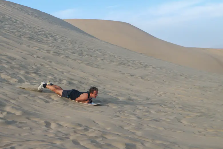 Sam sandboarding down a sand dune