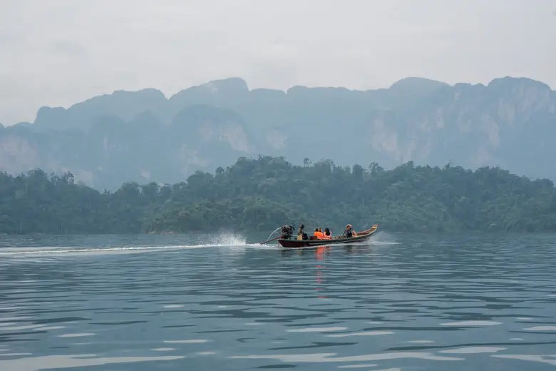 Boat driving along Cheow Lan Lake with limestone karsts in the background